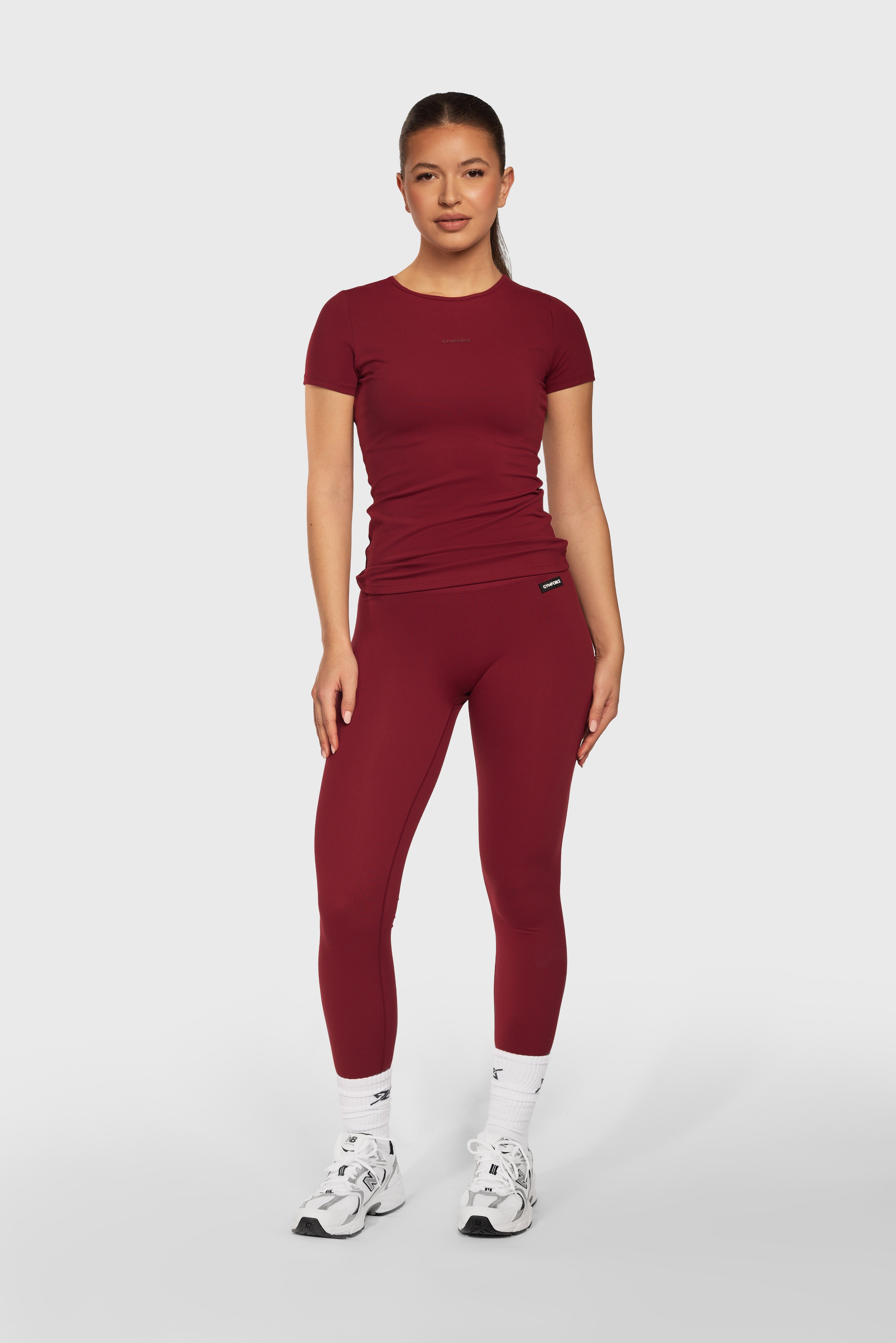 Model draagt het Burgundy Contour T Shirt en de Burgundy Contour Legging van Gymforce.